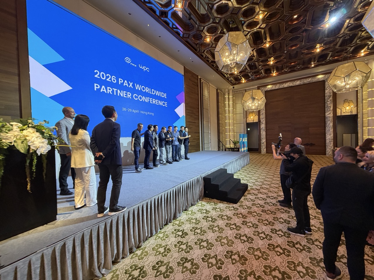 Conference participants lined up on a ballroom stage as photographers take pictures