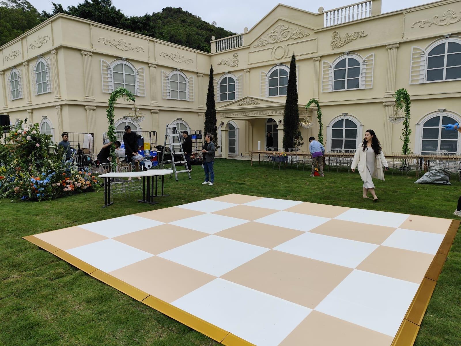 Checkerboard dance floor with white and beige panels set on the lawn outside a classical-style venue