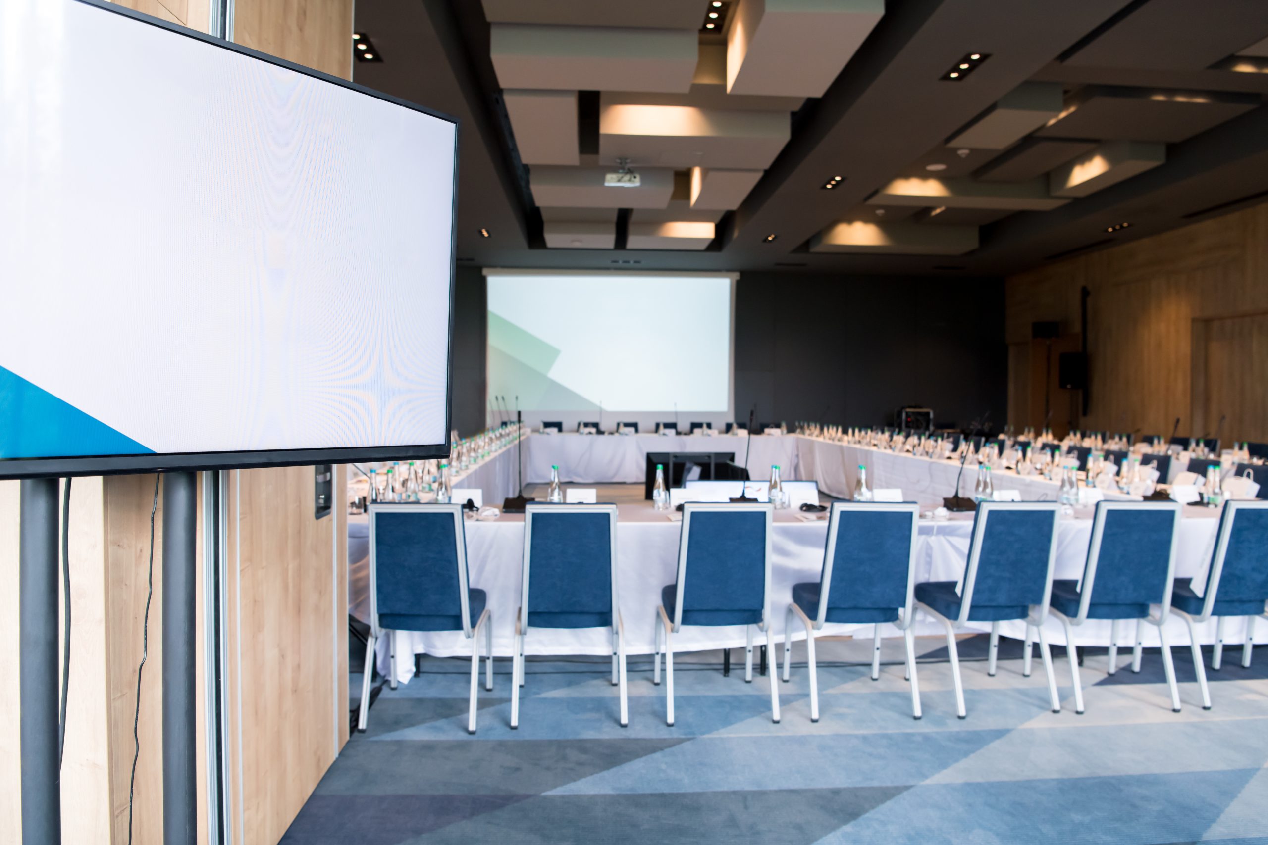 Conference room with a large TV, projection screen and U-shaped tables.